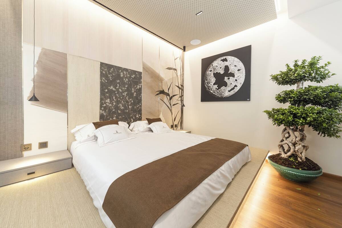 Une chambre moderne avec un grand lit, un arbre bonsai en pot et des œuvres d’art abstraites accrochées au mur.