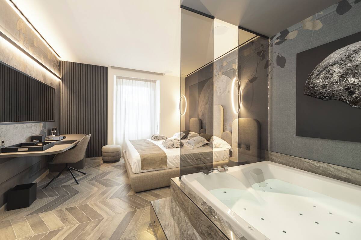Une chambre d’hôtel moderne dotée d’un grand lit, d’un coin salon avec un bureau, d’une baignoire et d’un grand miroir.