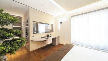 Une chambre d’hôtel moderne avec un plancher en bois, un lit, un bureau avec une chaise, un grand miroir et une plante en pot.
