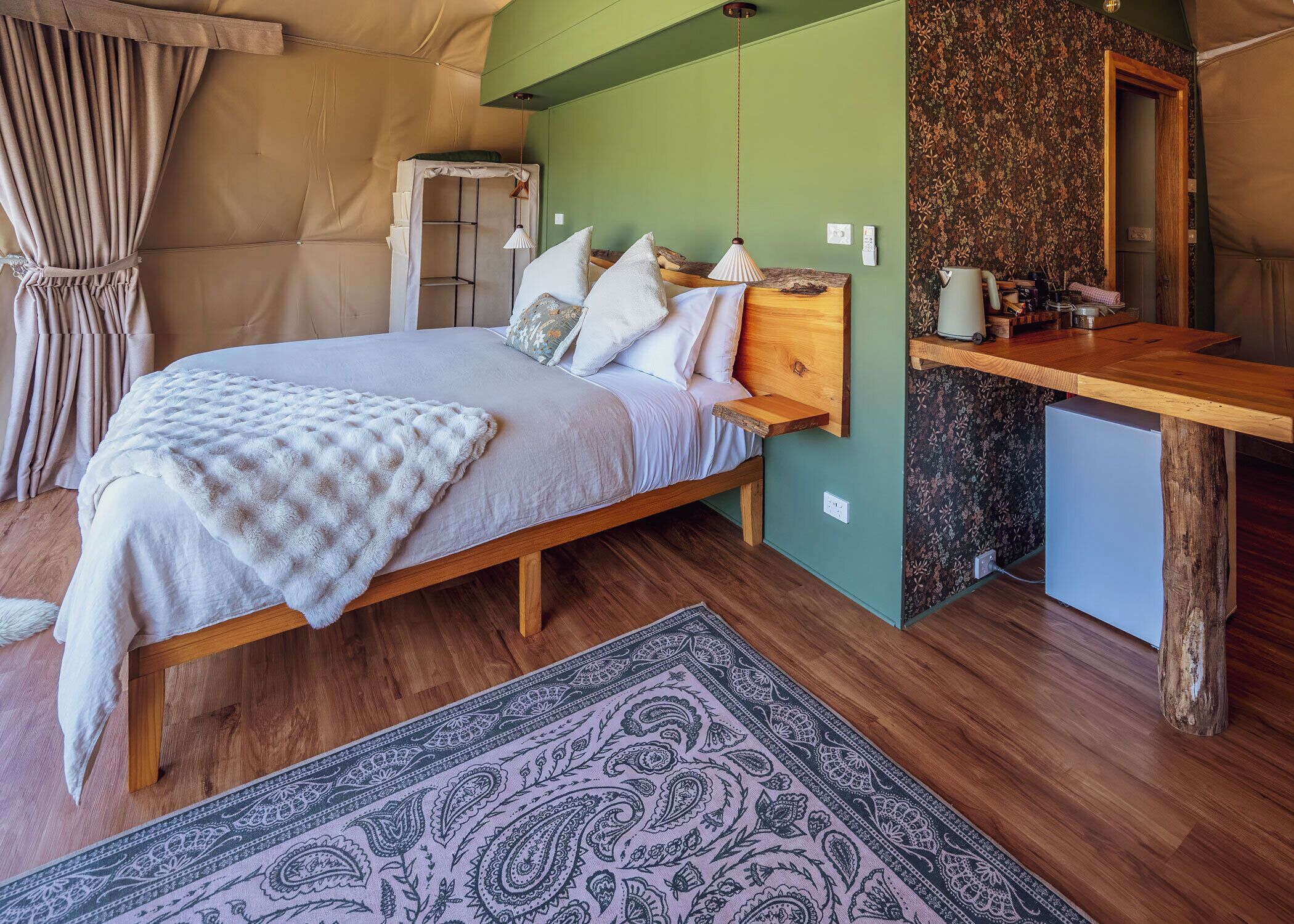 Un dormitorio acogedor con una cama de madera, un escritorio pequeño y una pared verde.