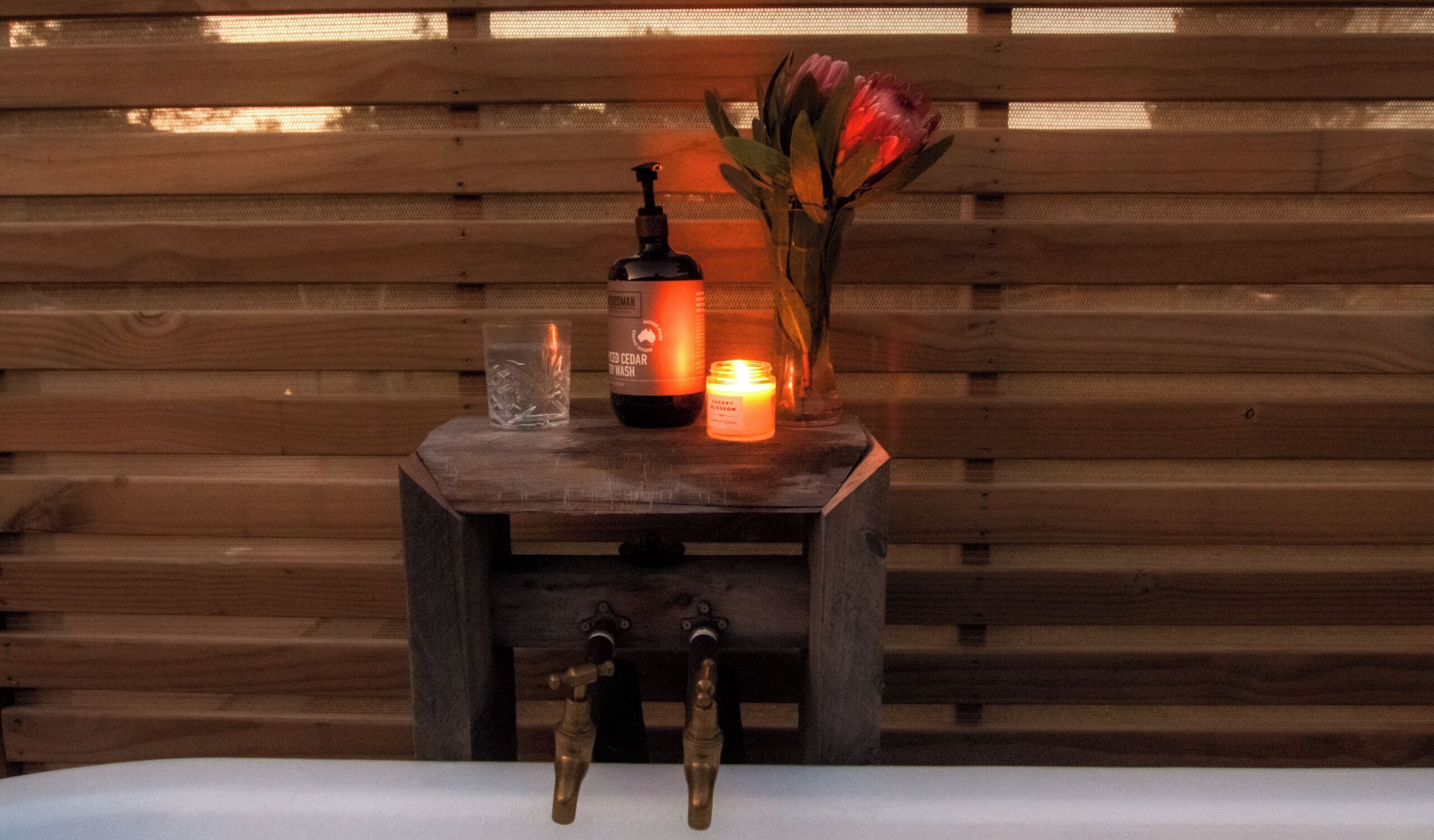 Un banco de madera con una vela, un vaso y una botella de jabón de manos.