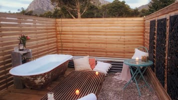 Un área de spa al aire libre con cerramiento de madera, una bañera antigua, una camilla de masaje y una mesa pequeña con velas.