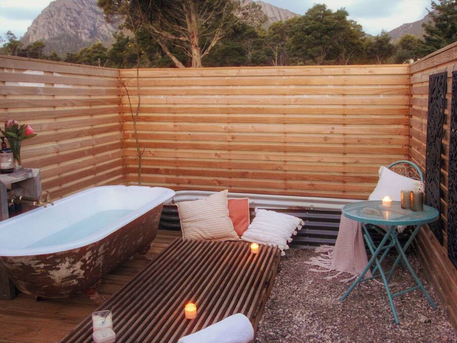 Un área de spa al aire libre con cerramiento de madera, una bañera antigua, una camilla de masaje y una mesa pequeña con velas.