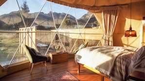 A bedroom with a large window, wooden furniture, and a view of mountains. - Wilder Tasmania (Gowrie Park)