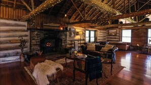 A log cabin interior with a stone fireplace, wooden furniture, and string lights. - Wilder Tasmania (Gowrie Park)