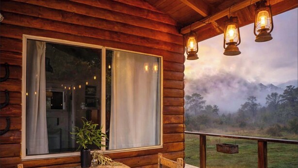 A wooden cabin with a large window, a wooden table, and three hanging lanterns. - Wilder Tasmania (Gowrie Park)