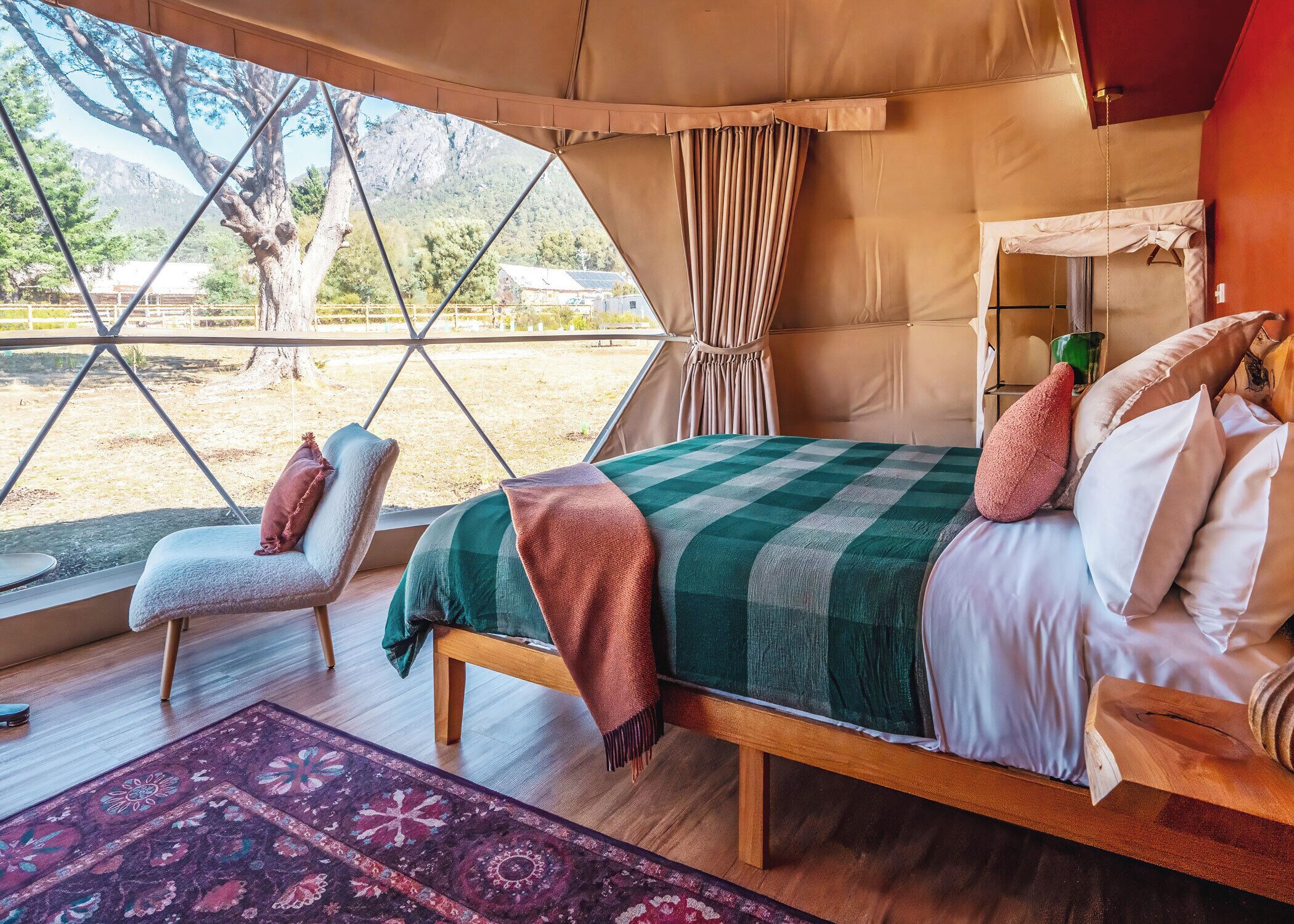 Une chambre aménagée sous une tente, comprenant un lit, une chaise et offrant une vue sur l’extérieur.