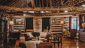 A rustic log cabin interior with a cozy fireplace, leather furniture, and string lights. - Wilder Tasmania (Gowrie Park)