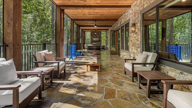 A covered outdoor area with stone flooring, wooden furniture, and large windows offering a forest view. - Iron Tree Lodge Blue Ridge GA (Blue Ridge)