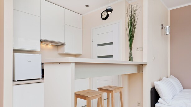 Habitación compacta con kitchenette, cama y un pequeño taburete de madera.
