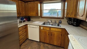 A kitchen with wooden cabinets, a stainless steel refrigerator, a dishwasher, a double sink, and a window with a view of the outside. - Charming retreat house (Spur)