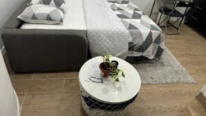 A compact bedroom with a sofa bed, a small round table with a plant, and a desk with a chair.