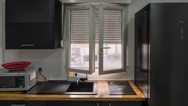 A compact kitchen with a microwave, a sink, a window with blinds, and a refrigerator.