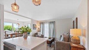 A modern living room with a sofa, a coffee table, and a lamp. There is a dining area with a table and chairs.