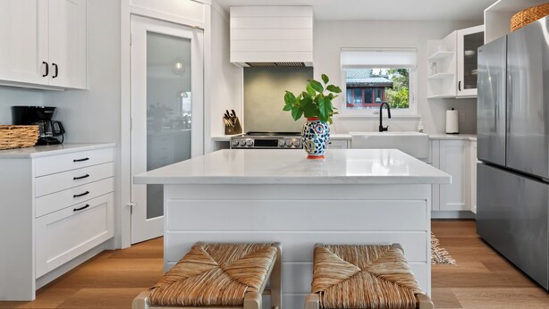 A modern kitchen with white cabinetry, a large island, two hanging pendant lights, and a stainless steel refrigerator.