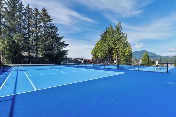 An outdoor tennis court with a blue surface, surrounded by tall trees and a clear sky. - Downtown Tofino Bungalow-Tonquin,Restaurants,Tours (Tofino)