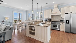 A modern kitchen with white cabinetry, a central island, stainless steel appliances, and a view to the outside. - Outdoor TV, Bikes, Gulf Views, Prime 30A Location, Large Private Pool (Santa Rosa Beach)