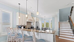 A modern kitchen with a central island, white cabinetry, and a wooden staircase. - Outdoor TV, Bikes, Gulf Views, Prime 30A Location, Large Private Pool (Santa Rosa Beach)