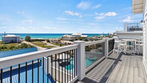 A wooden deck with a pool, white railings, and a view of the ocean and beach houses. - Outdoor TV, Bikes, Gulf Views, Prime 30A Location, Large Private Pool (Santa Rosa Beach)