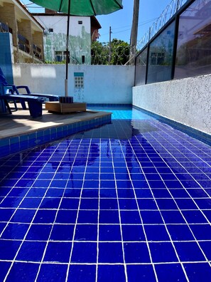Une piscine aux carreaux bleus, une terrasse en bois et un parasol vert.