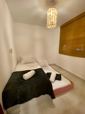 A modern bedroom with a bed, pillows, a black blanket, and a unique hanging light fixture. - Flat 10 Residencial Praça 19 by La Playa (Ipojuca)