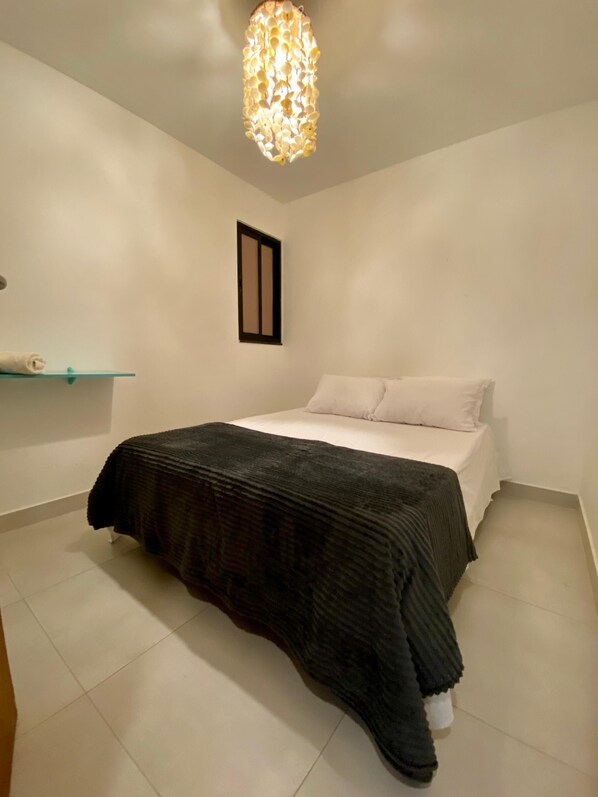 Une chambre à coucher avec un lit, un luminaire suspendu et une petite fenêtre.