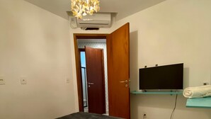 A bedroom with a bed, a TV mounted on the wall, and an open door leading to another room.
