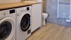 A modern laundry room with a washing machine and dryer, a sink, and a towel rack. - Le Champ du Roy (Chasse-sur-Rhône)