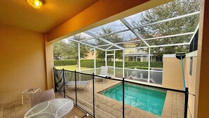 A covered outdoor area with a pool, a table, and chairs.