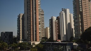 Un paisaje urbano con edificios residenciales altos, un edificio moderno con fachada geométrica y un cielo azul despejado.