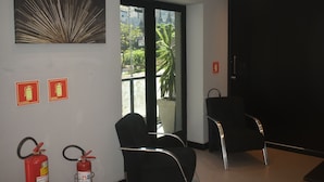 Habitación de hotel moderna con un ventanal grande, dos sillas negras y dos extintores de incendios montados en la pared.