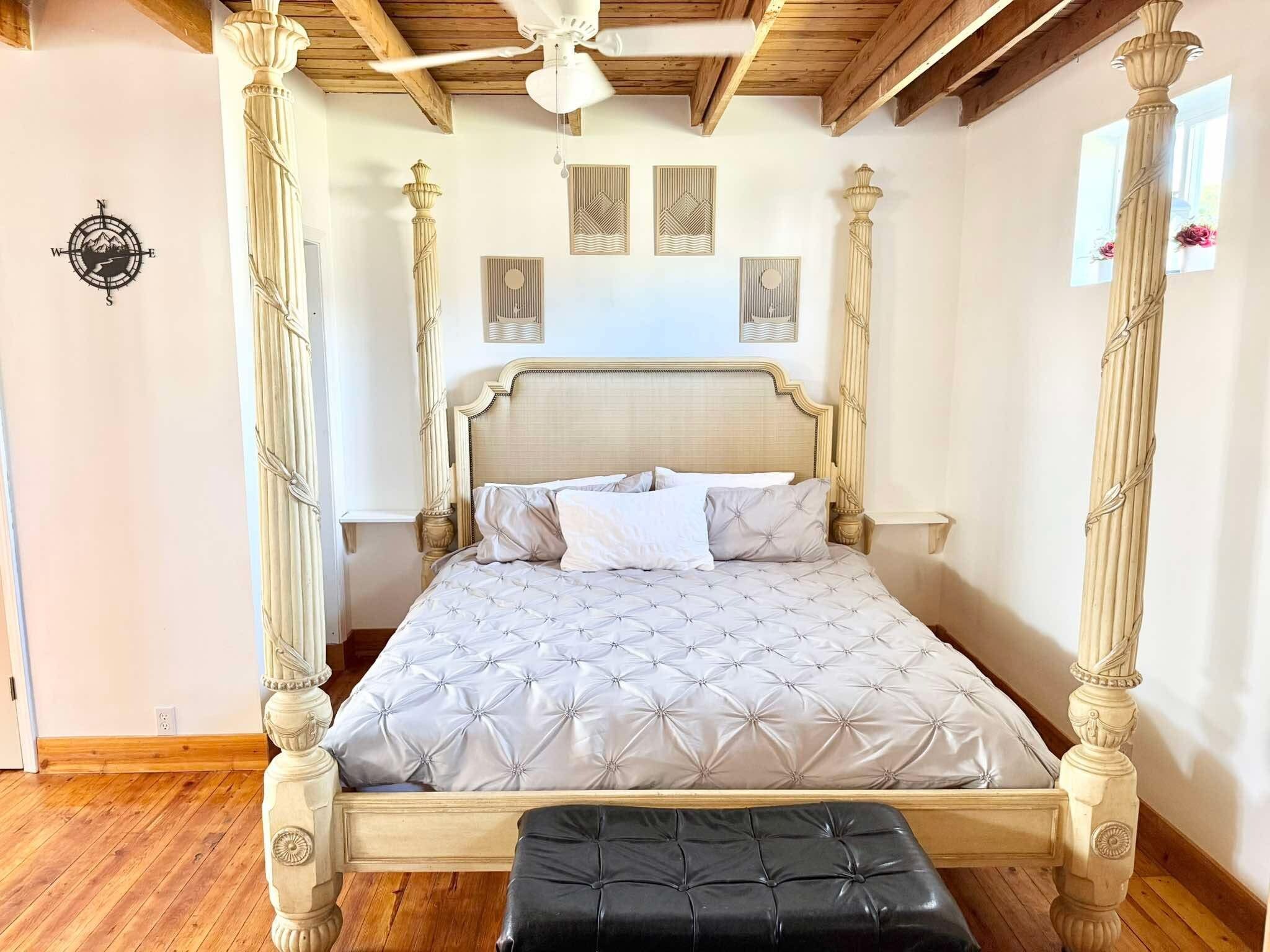 A four-poster bed with a tufted headboard and a matching bench, in a room with wooden beams and decorative wall panels.