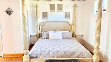A four-poster bed with a tufted headboard and a matching bench, in a room with wooden beams and decorative wall panels.