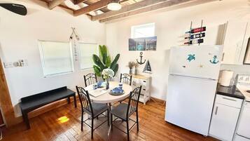 A compact kitchen with a white refrigerator, wooden flooring, and a dining table with chairs.