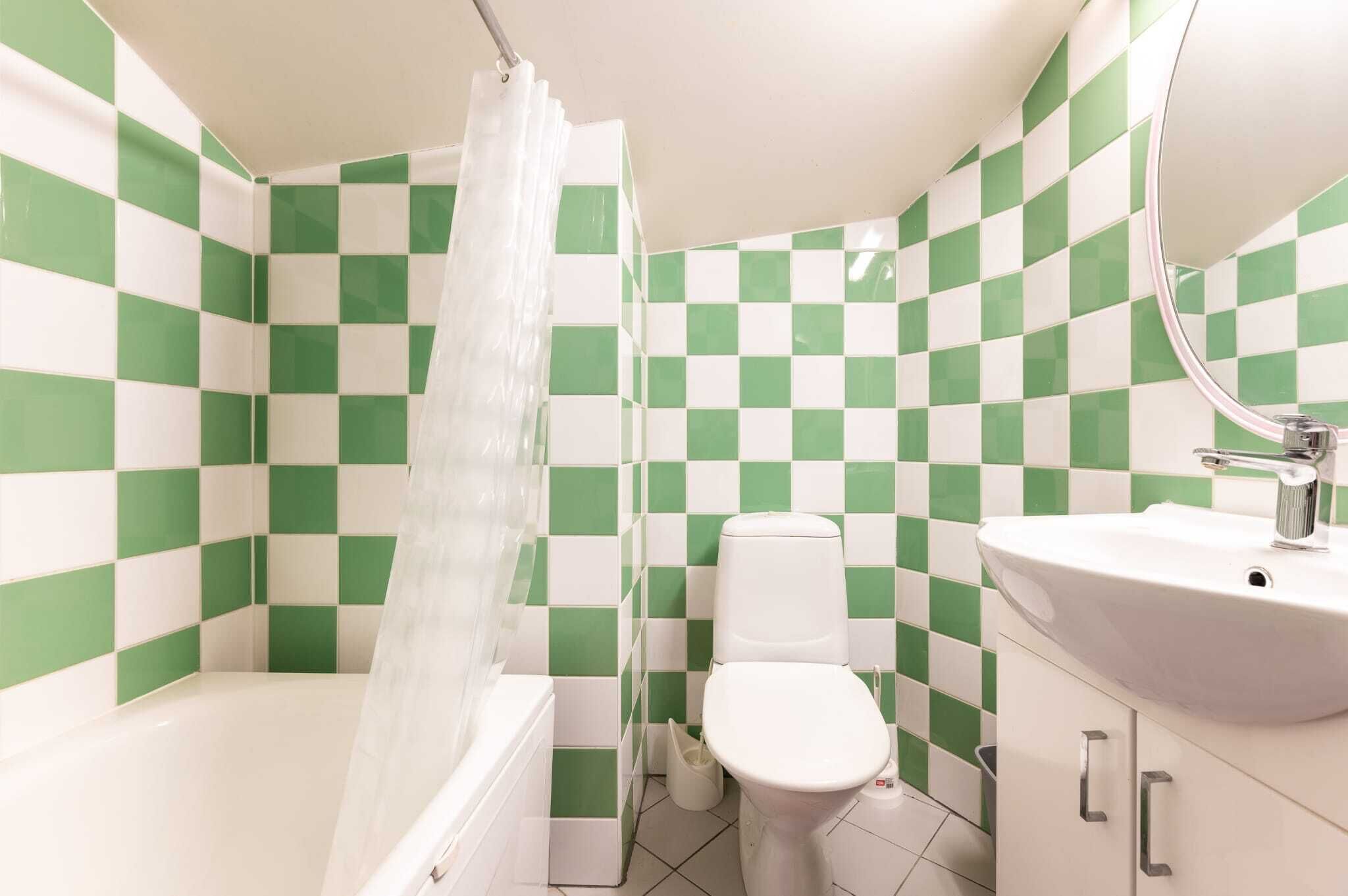 Une salle de bain avec des carreaux verts et blancs formant un motif à damier, des toilettes blanches, un lavabo blanc et un rideau de douche.