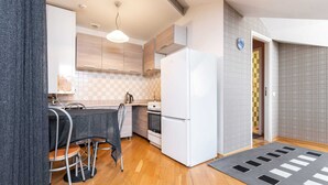 A compact kitchen with wooden cabinets, a white refrigerator, a small oven, and a bar area with stools. - DICTUMFACTUM RESIDENCE 2BedRoom (Tallinn)