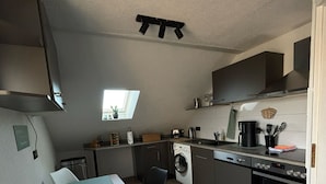 A compact kitchen with a dining area, a washing machine, and a built-in oven. - Gemütliche Naturnahe Ferienwohnung in Oberbayern "Am Weiher" (Denklingen)