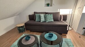 A cozy living room with a dark brown sofa, two side tables, and a small round table with a blue bowl. - Gemütliche Naturnahe Ferienwohnung in Oberbayern "Am Weiher" (Denklingen)