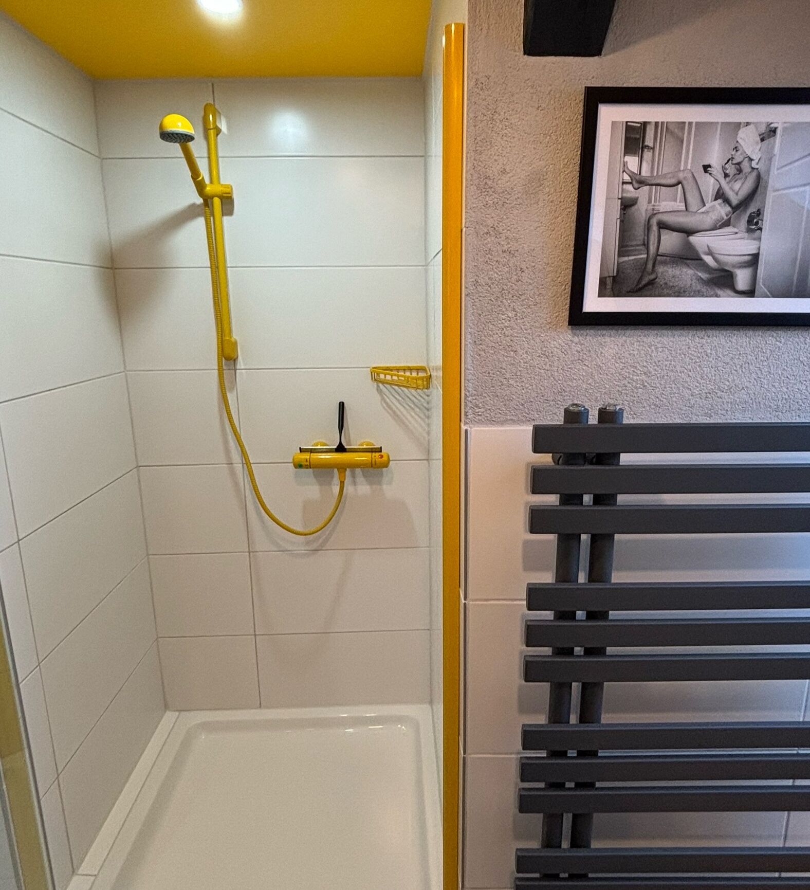 A shower with yellow fixtures, a white tiled wall, and a framed picture on the wall.