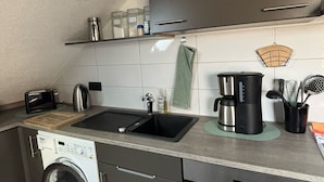 A compact kitchen with a washing machine, a coffee maker, and a toaster. - Gemütliche Naturnahe Ferienwohnung in Oberbayern "Am Weiher" (Denklingen)