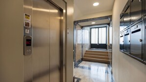 An elevator with a digital display, a marble staircase, and a door leading to a room with a large window and a door with a metal handle.