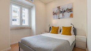 Une chambre à coucher avec un lit, deux tables de chevet, une fenêtre et un tableau au mur.