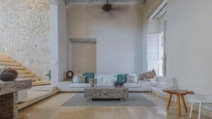 A spacious living room with a stone coffee table, a white sofa with teal cushions, and a wooden side table. - Casa Charlies Can (Cartagena)