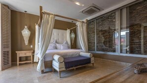 A four-poster canopy bed with a headboard, a bedside table, and a view of the outside through a large window. - Casa Charlies Can (Cartagena)