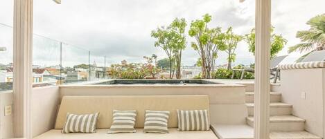A rooftop terrace with a beige sofa, striped cushions, and a view of the cityscape and greenery.