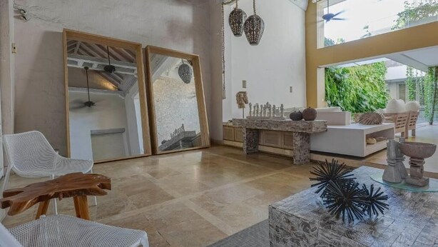 A spacious living area with a large window, a wooden coffee table, and a seating arrangement including a white chair and a sofa. - Casa Charlies Can (Cartagena)