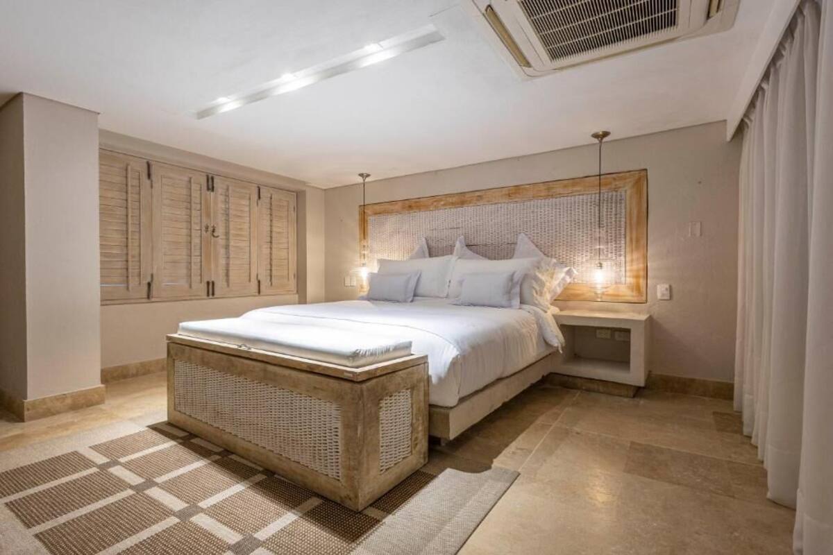 Una camera da letto con un letto, comodini, una panca in vimini e un'ampia finestra con tende.