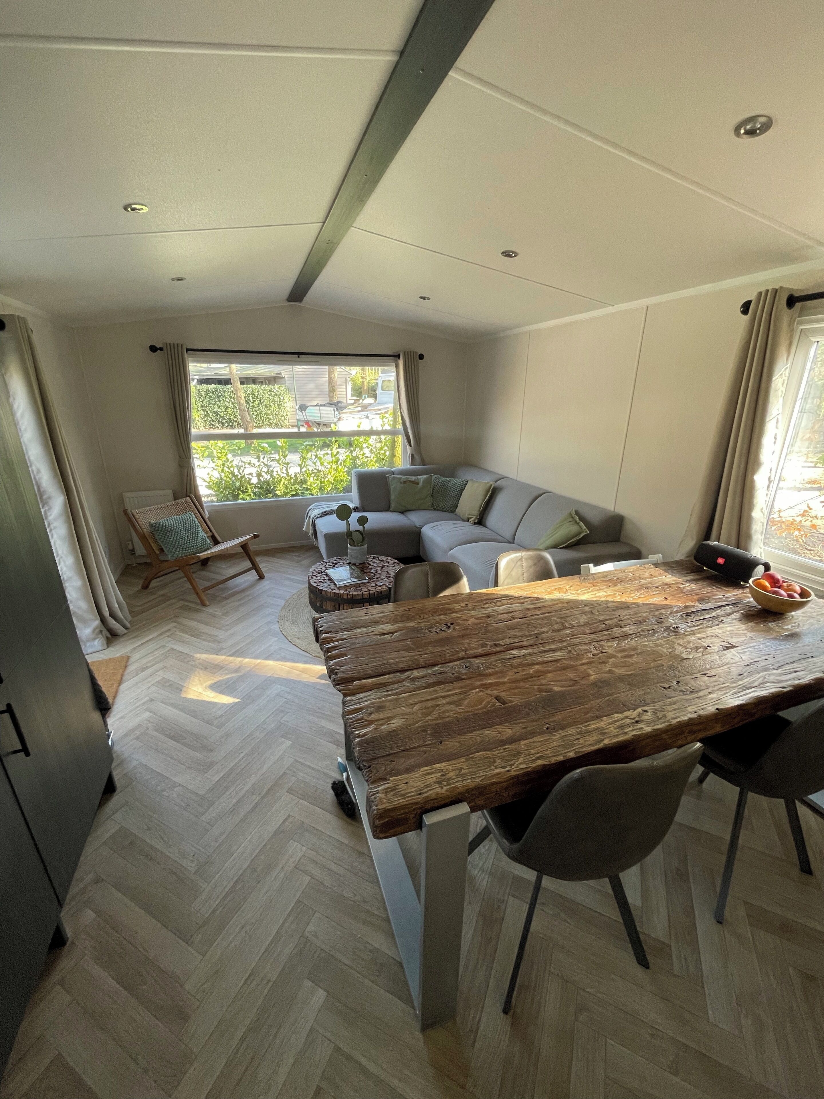 A modern living room with a wooden dining table, a sofa, and a window with a view of greenery.