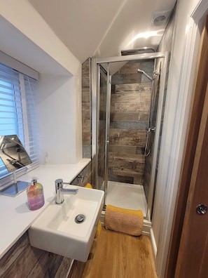 Un baño moderno con cabina de ducha de vidrio, un lavamanos blanco y suelo de madera.