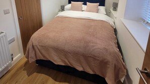 Une chambre à coucher avec un lit, une porte en bois, un radiateur blanc et une fenêtre avec des stores.
